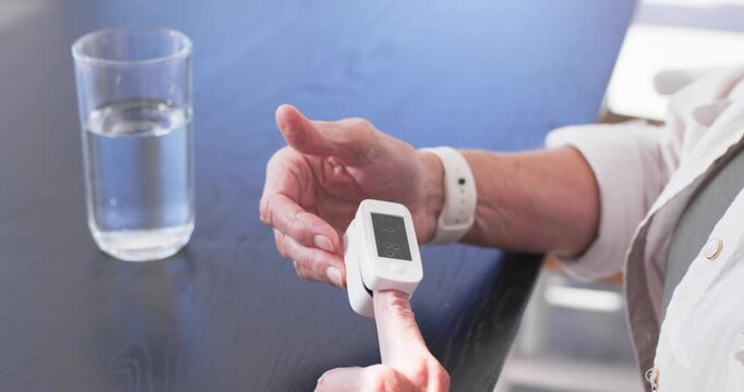 Senior woman aligning finger into fingertip oximeter on dark wooden table, checking oxygen level