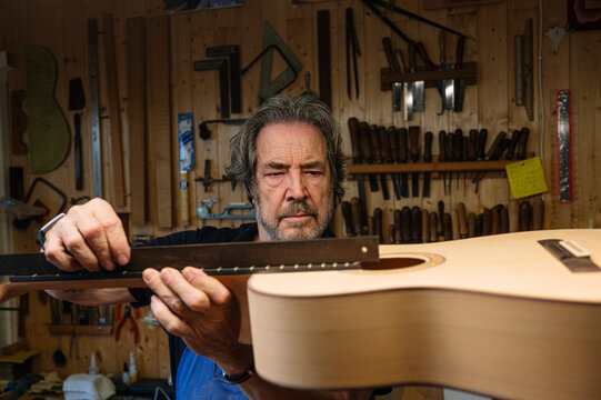 Skilled craftsman measuring guitar in workshop