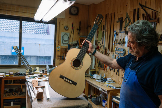 Craftsman examining guitar in woodworking workshop