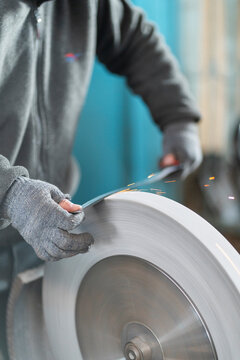 Industrial worker grinding metal on large rotating wheel