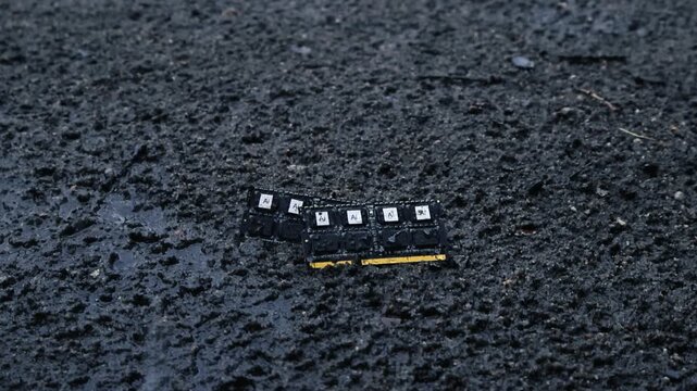 Discarded computer memory chips with AI logos getting wet from raindrops falling on dark, muddy ground, symbolizing technological waste, data loss, and environmental pollution