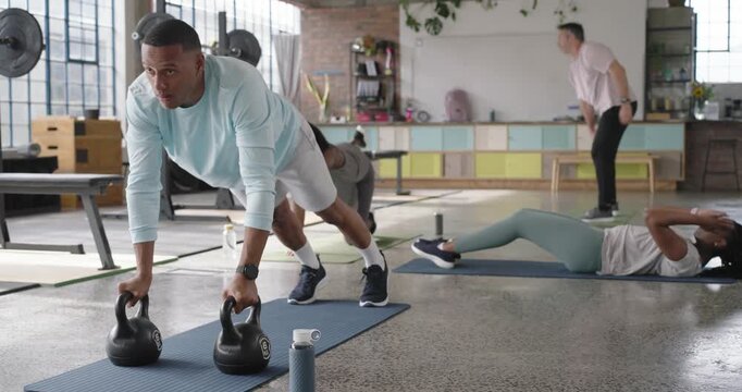 Diverse class starting circuit at loft gym, man doing kettlebell plank rows on mats for core