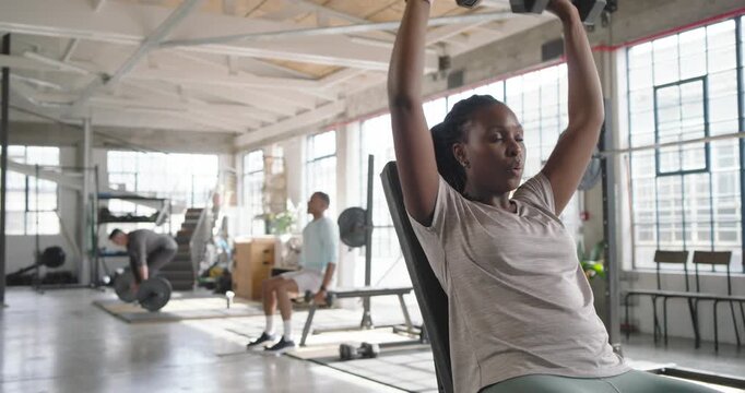 African American woman holding DBs pressing incline bench in loft gym training or resting, copy spac