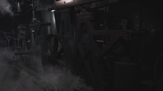 Dark engine alcove shrouded in smoke and soot, niche wheel and axle silhouettes barely visible, drip stains and weld scars mark long neglect, salvage assessment