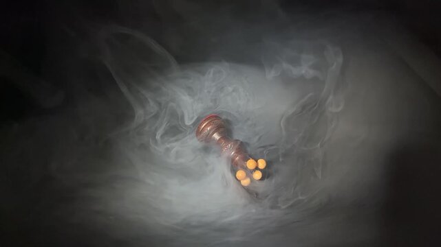 Human hand knocking over dark wooden chess queen in dramatic smoke on black background. Concept of defeat, overthrow, power, disruption and business failure.