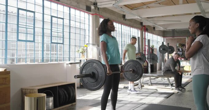 Female lifter walking to loaded barbell at gym gripping lifting for strength highfiving spotter
