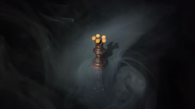 Human hand knocking over dark wooden chess queen in dramatic smoke on black background. Concept of defeat, overthrow, power, disruption and business failure. Slow motion 4K video.