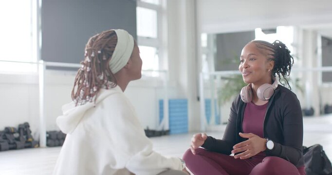 African female friends sitting on mats, maroon woman with headset starting chat, catching up