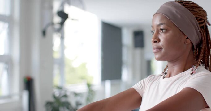 Adult African American woman gripping, raising weights to eye level in gym, training, copy space