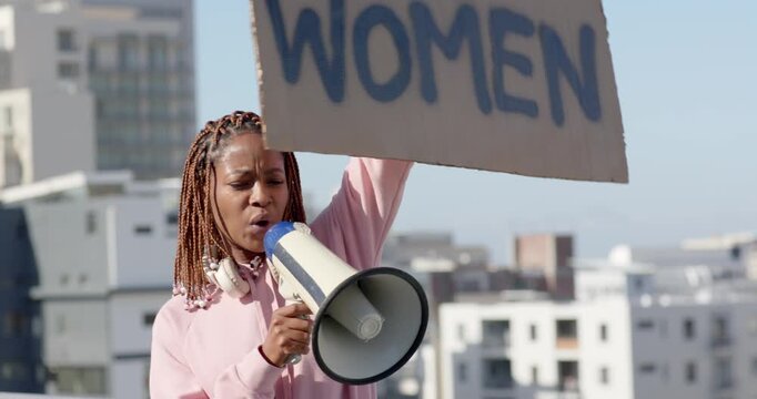 Responding to rally, woman on rooftop holding WOMEN sign and speaking into megaphone for rights