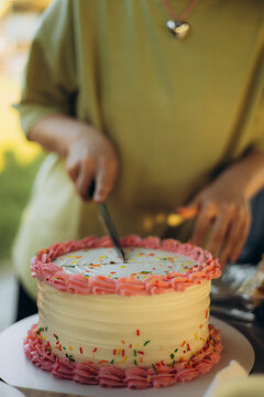 Person slicing colorful frosted birthday cake at celebration