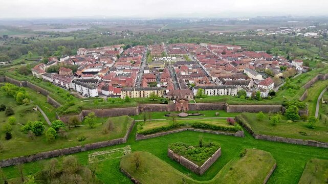 Aerial drone view of star fortress bathed in gentle morning mist with dawn light softly illuminating ramparts and terracotta rooftops. Atmospheric haze clinging to bastion points and moat creating