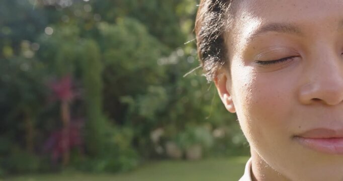 African-American woman facing yard reacting to sun blinking opening smiling by shrubs, copy space