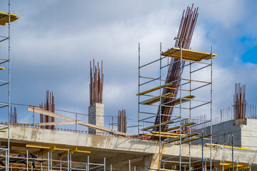 High Rise Building Construction Site Featuring Exposed Steel Rebar Columns and Metal Scaffolding Platforms Under Cloudy Blue Sky During Urban Development Project Work © sommersby