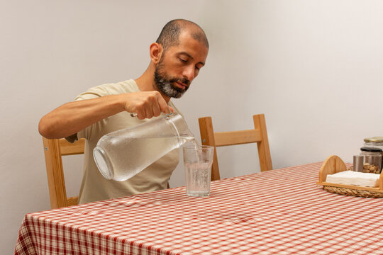 Hispanic man pouring cold water into a glass during summer heatwave at home