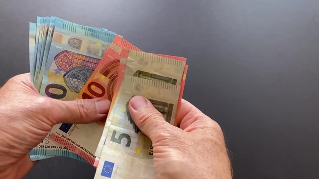 A mans hands counting out euro notes then a female hand stretches out to receive some off it against a dark background
