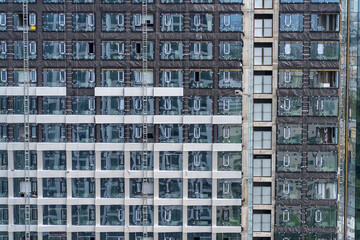 Obraz premium Modern high-rise building under construction featuring repetitive geometric grid of glass windows and structural steel frames creating industrial urban architectural texture pattern
