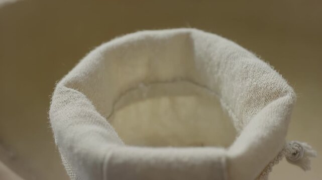 Close-up of white granulated sugar being poured from a wooden spoon into a fabric bag, showcasing the continuous flow of sugar in a kitchen setting