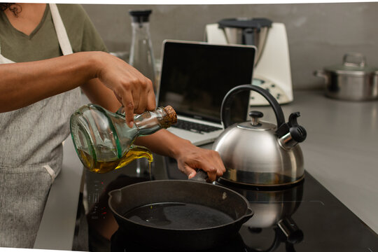 Close up of olive oil being poured into cast iron skillet in modern kitchen
