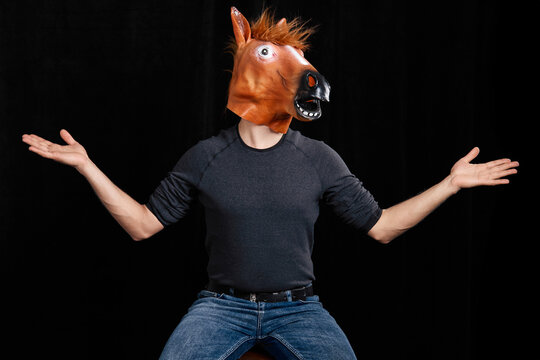 Man wearing horse mask shrugging with arms raised isolated on black background