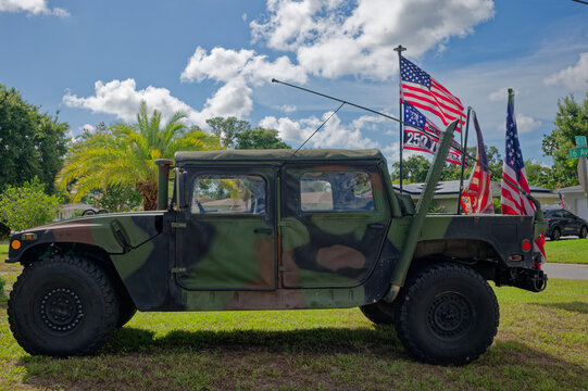 Camouflaged military Humvee (HMMWV) parked on a suburban lawn with several American flags and banners. Editorial Use Only July 5, 2026 St. Petersburg , FL USA. Evoking patriotism, veterans, and milita