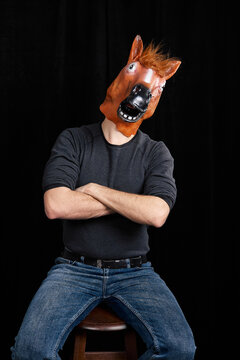 Man wearing horse mask sitting with crossed arms isolated on black background