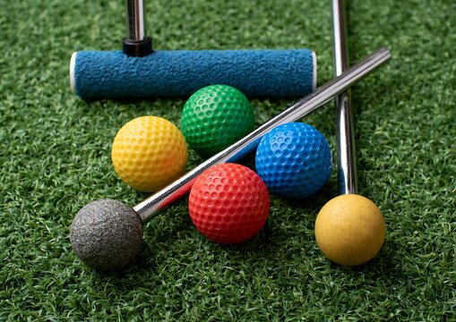 Miniature golf equipment including colorful golf balls and putters on artificial green grass turf