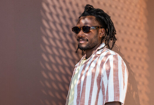 Cuban man in sunglasses posing by sunlit terracotta wall