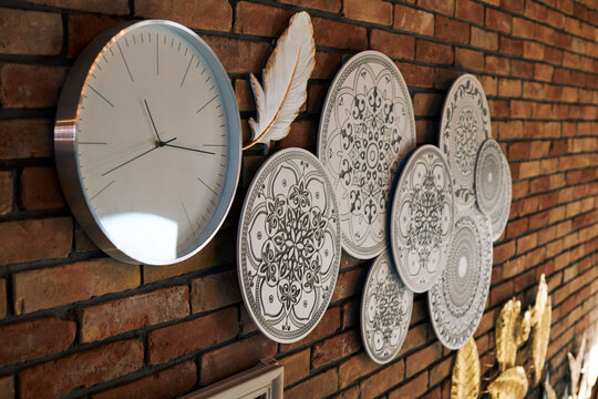 Modern wall clock with decorative ceramic plates on rustic brick interior background display