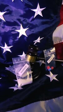 Conceptual footage of a judge's gavel and evidence bags containing illicit drugs resting on the flag of the United States of America, symbolizing the nation's fight against substance abuse