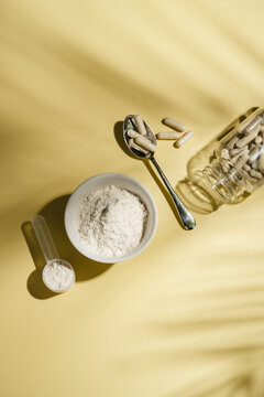 Collagen powder, capsules and scoop on yellow background with sun light and dark shadows, food supplement concept