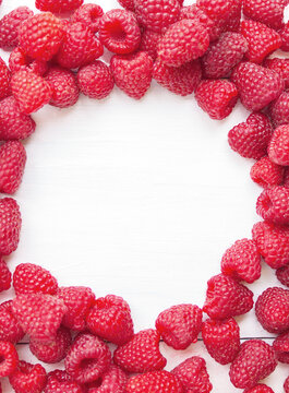 A top view frame of fresh red raspberries arranged on a white wooden background with empty copy space.