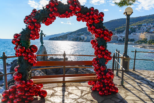 Red Christmas ornament arch framing the Maiden with the Seagull statue on the waterfront in Opatija, Croatia