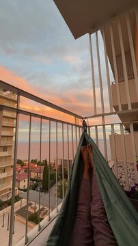 Relaxing in a hammock on a balcony with colorful sunset sky. Cozy evening atmosphere representing slow living