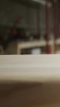 Vertical video: Leaning man in red plaid shirt inspecting board, blowing dust in shop, copy space