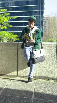 Vertical video: Arriving man in beanie leaning on low ledge, placing coffee, studying green folder