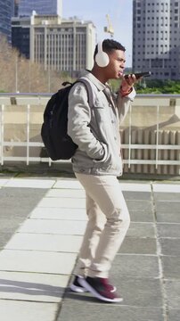 Vertical video: Entering left, man commuting walking talking checking phone at plaza jacket headset