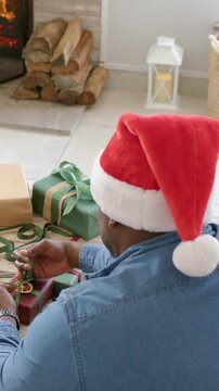 Vertical video: Tying man in Santa hat sorting gifts at home, turning to sound, with green ribbon