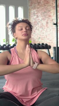 Vertical video: Starting with hands overhead woman in pink top breathing on green mat, rack visible