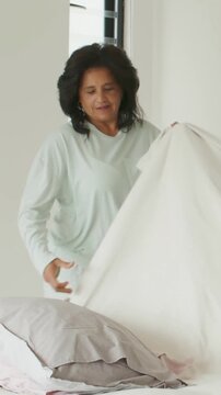 Vertical video: Unfolding duvet woman in mint PJs making bed at home smoothing gray pillow neatly