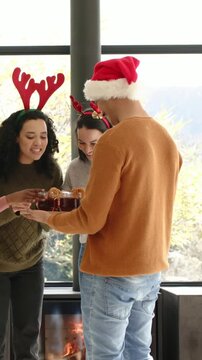 Vertical video: Entering Santa-hat man with tray by window, giving holiday mugs to antlered friends