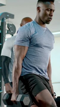 Vertical video: Holding hex weights, man doing lunges in gym for strength, in tee, coach watching