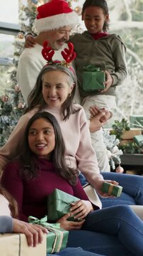 Vertical video: Sharing green gifts for Xmas, family leaning on sofa at home wearing Santa hats