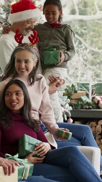 Vertical video: Laughing family holding green gifts on couch for Xmas as camera pans, in Santa hat