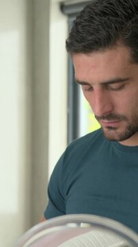 Vertical video: Placing cream dots, man in teal tee massaging face at vanity for skin, table mirror