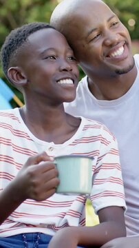 Vertical video: Seeing dad enter boy turning smiling dad leaning caring holding blue mug in park