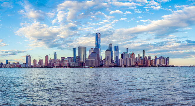 Wide-angle panoramic view of the iconic New York City skyline in the early evening, captured from the waterfront in Jersey City, New Jersey, across the Hudson River.