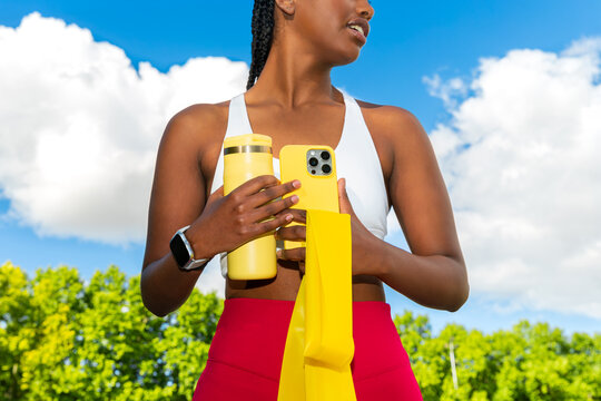 Gen Z black woman in sporty outfit holding phone outdoors