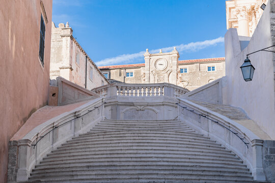 Historic Baroque limestone staircase in the historic old town of Dubrovnik, Croatia, captured during a very peaceful morning sunrise with a clear blue sky and absolutely no people in the camera frame.