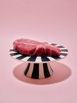 Raw beef steak on a striped platter with pink backdrop